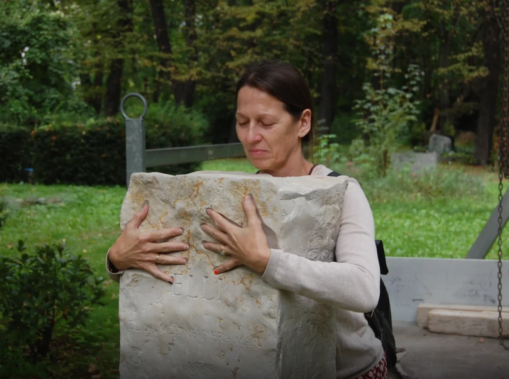 Frau umarmt einen Grabstein und legt ihre Hände in eingearbeitete Vertiefungen