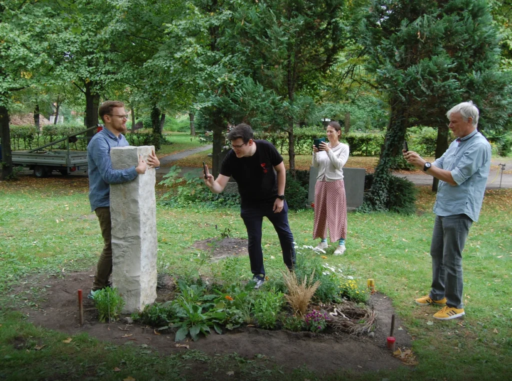 Mann umarmt Grabstein mit Handabdrücken, umgeben von einer Gruppe Menschen