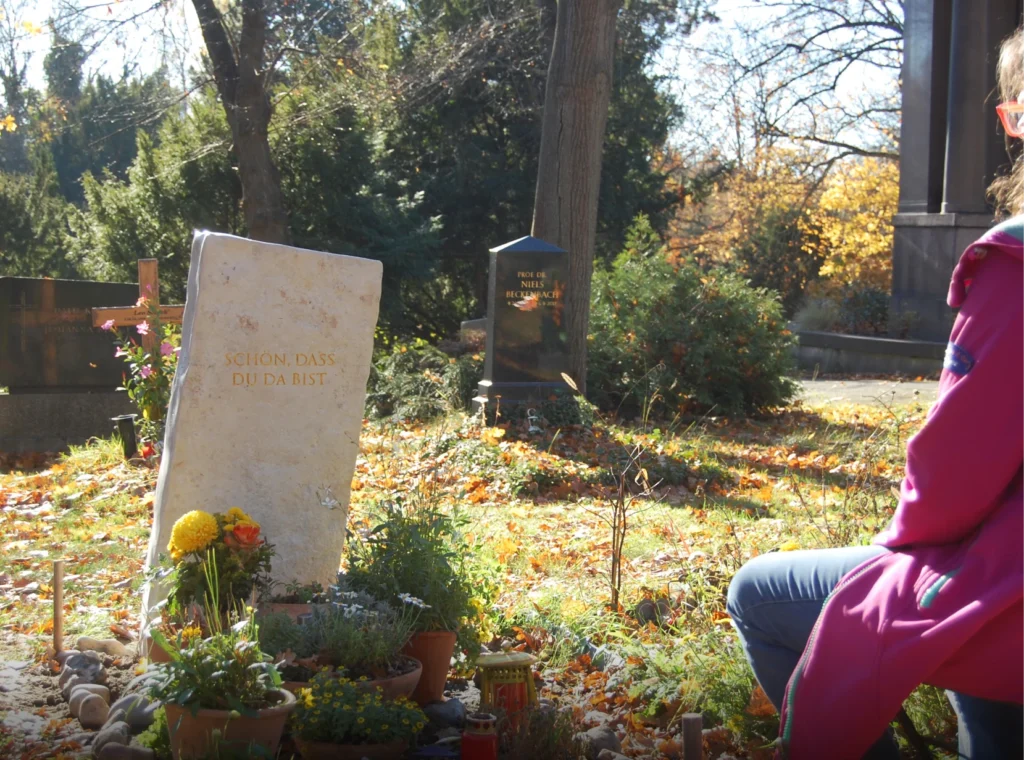 Grabmal „Ein denkwerk für Ercan Freiherr von Moreau“ mit sitzender Angehöriger im Vordergrund von Michael Spengler