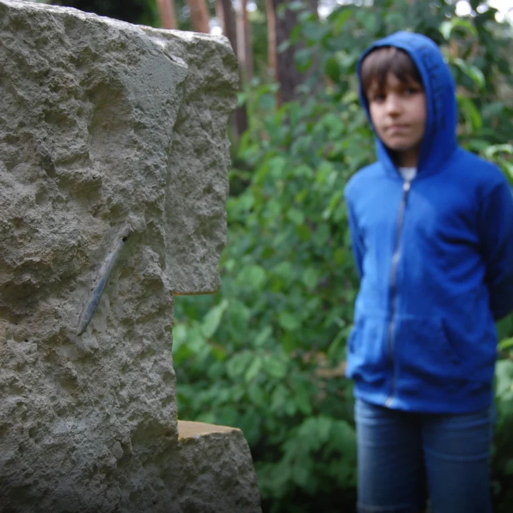 Grabstein aus Kalkstein mit herausgearbeitetem orthodoxen Kreuz und vergoldeten Flächen, davor ein Junge