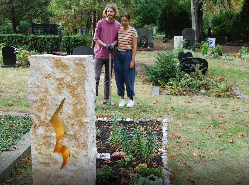 Rückansicht des Grabmals „Ein denkwerk für Jutta Petermann“ mit zwei Personen davor von Michael Spengler