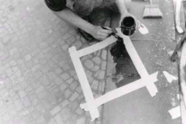 Ein Naturstein im Straßenpflaster wird mit grafithaltiger Farbe für einen Abdruck beim Kunstprojekt „ge(h)steine – topolithografia“ von Michael Spengler vorbereitet