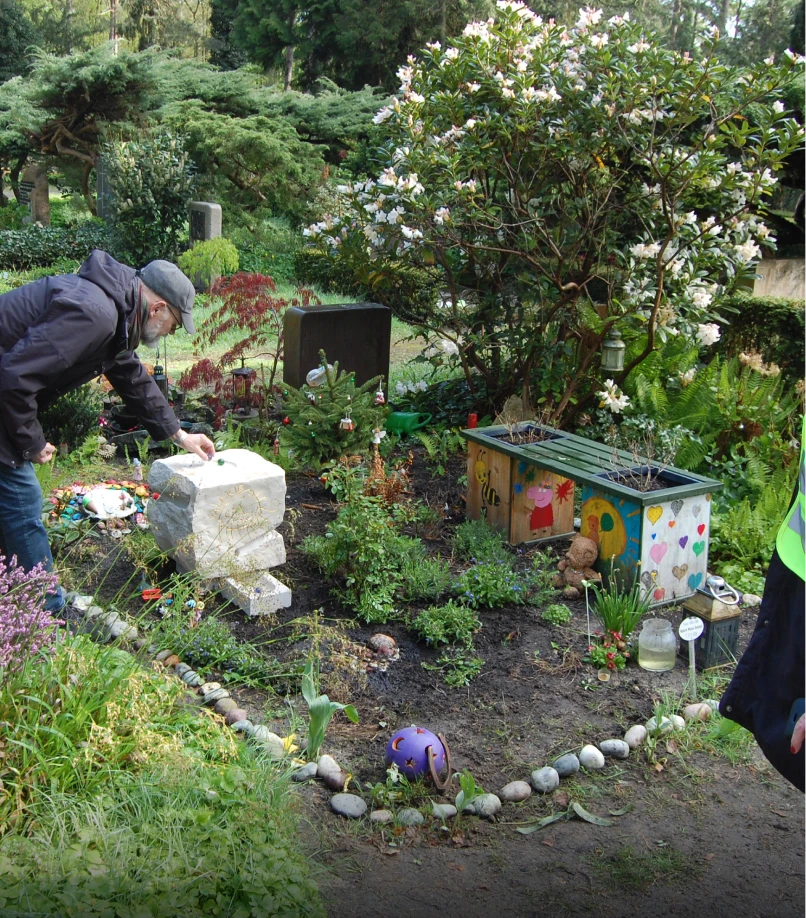 Angehöriger legt eine Glasmurmel auf das Grabmal „Ein denkwerk für Valerie“ von Michael Spengler