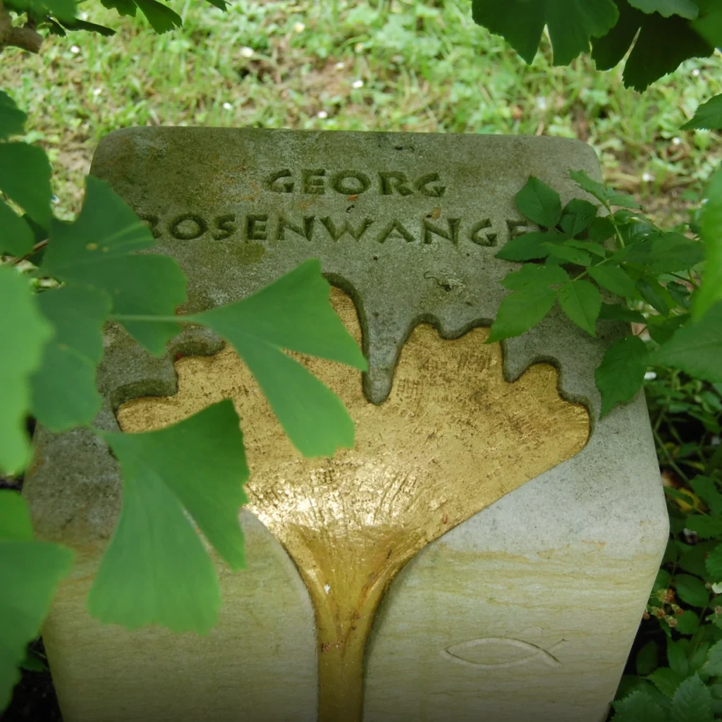 Vogelperspektive auf den Sandstein-Grabstein mit vergoldetem Ginkoblatt