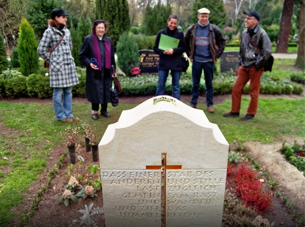 Grabstein von hinten angeschnitten mit davor stehender Personengruppe