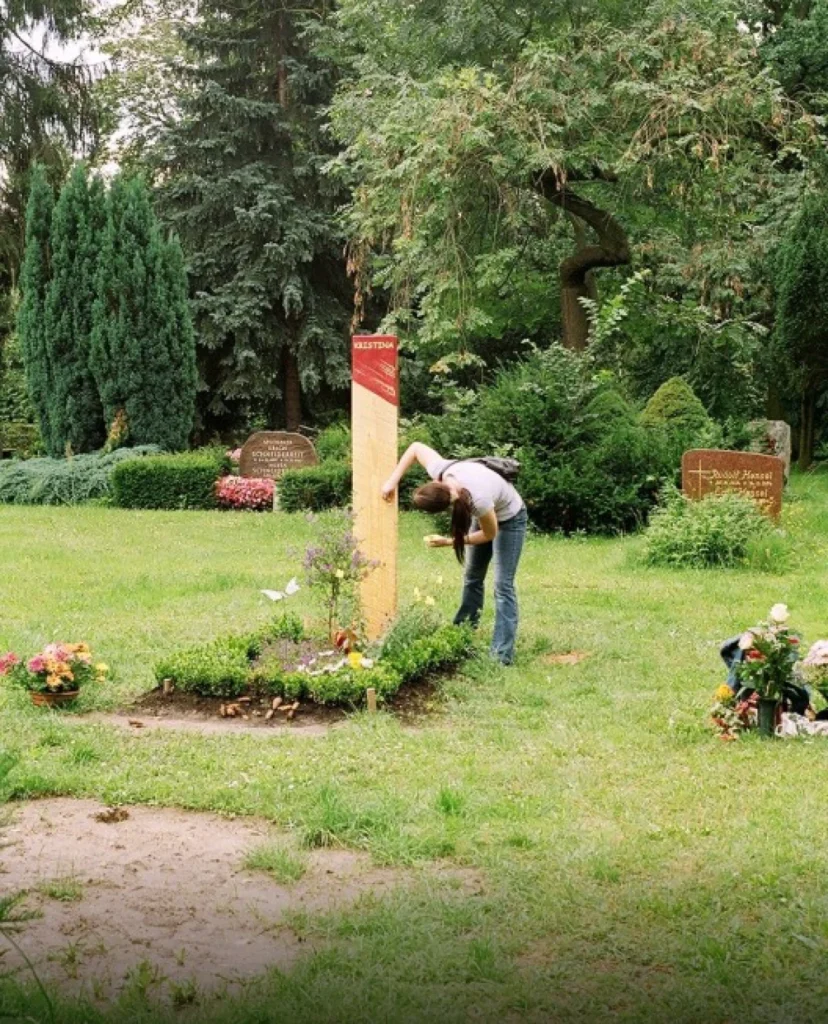 Provisorischer Grabstein aus Holzbrett mit roter Spitze und Schriftzug