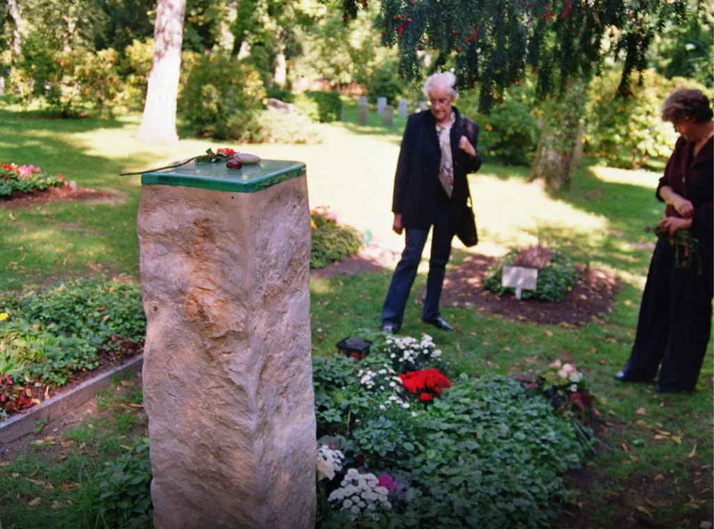 Angehörige betrachten das Denkwerk für Gerhard Petschel-Held von hinten angeschnitten