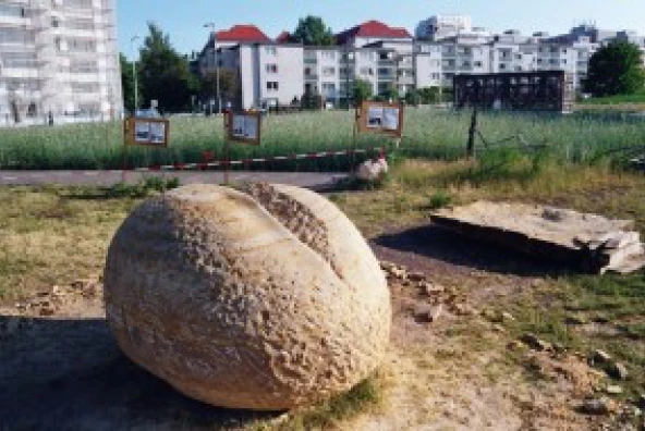 Fertige Schrippen-Skulptur aus Sandstein vor einer Werkstatt, umgeben von Roggenfeld