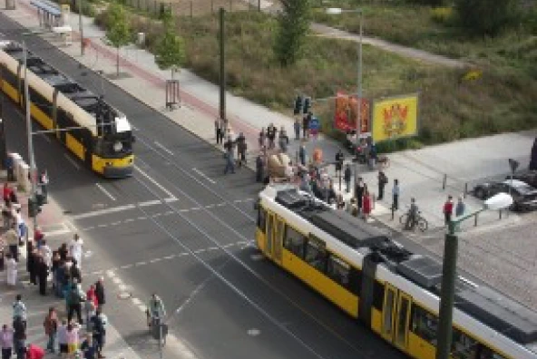 Straßenbahn hält an, während eine große Sandstein-Schrippe über die Bernauer Straße transportiert wird